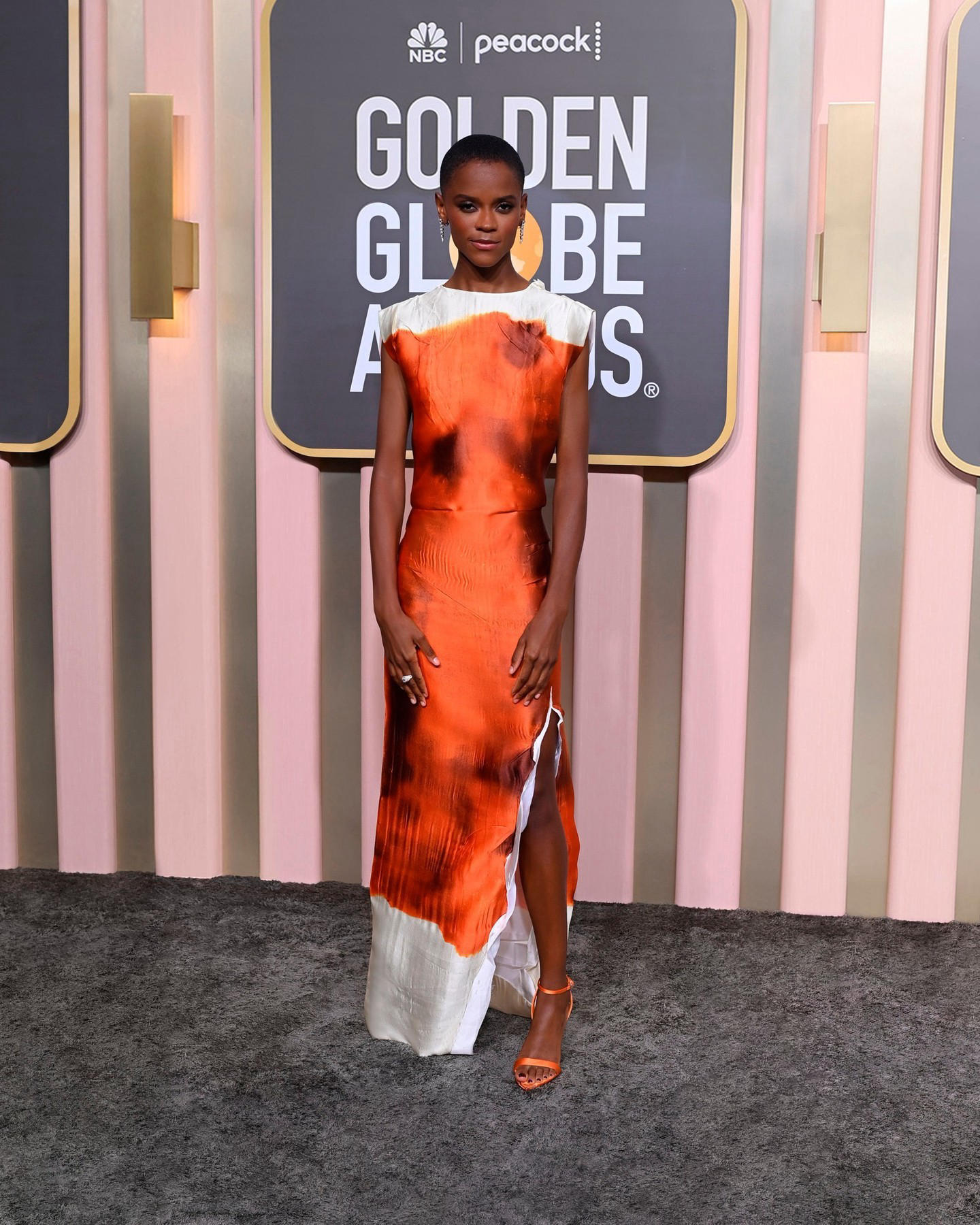 Letitia Wright wore a #Prada orange and cream printed satin dress with slit and wide neckline on the
